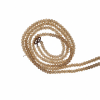 A detailed view of a necklace chain made from small, faceted champagne-colored crystal glass beads, shown coiled against a white background with a dark metal hook clasp.