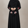 A fashion model wearing a full-length black abaya and matching hijab with maroon and white floral embroidery details.