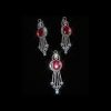 A sparkling jewelry set featuring a pendant and earrings with large oval red rubies surrounded by shimmering diamonds on a black background.