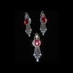 A sparkling jewelry set featuring a pendant and earrings with large oval red rubies surrounded by shimmering diamonds on a black background.