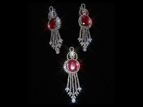 A sparkling jewelry set featuring a pendant and earrings with large oval red rubies surrounded by shimmering diamonds on a black background.