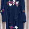 The backside of a black abaya showing a large horizontal floral applique design across the upper back and ruffled fabric panels.