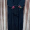 Front view of a black abaya hanging on a rack with bell-style sleeves featuring maroon and brown floral patches.