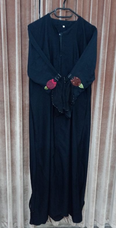 Front view of a black abaya hanging on a rack with bell-style sleeves featuring maroon and brown floral patches.