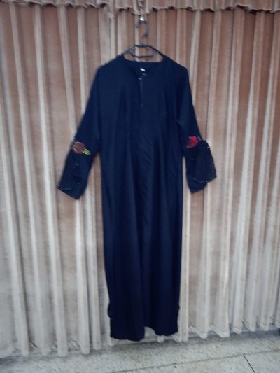 Full-length view of a simple black abaya with long sleeves and delicate floral applique accents.
