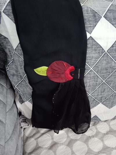Close-up shot of an abaya sleeve cuff showing a maroon fabric flower with a green leaf and stone embellishments.
