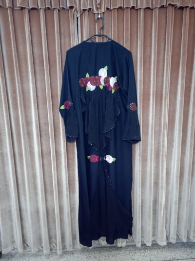 Rear view of a black abaya on a hanger, highlighting the ruffled back detailing and floral applique work.
