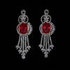 Close-up shot of elegant silver dangle earrings with central oval red gemstones and intricate diamond-studded floral patterns.