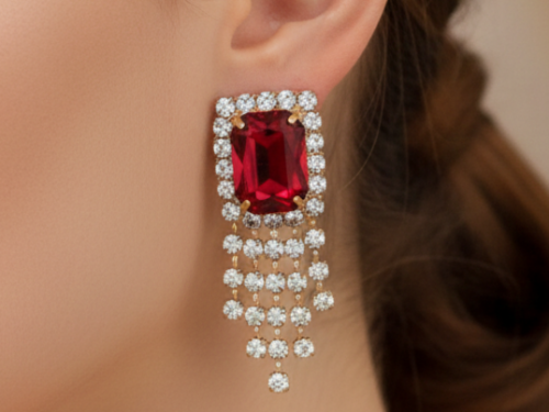 A close-up of a model wearing a large emerald-cut ruby earring surrounded by diamonds with a cascading diamond fringe.