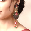 Close-up of a woman's profile wearing a large, traditional red and gold statement earring with a maroon and gold silk saree.