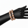 Two rose gold bangles displayed on a black mannequin hand. The design features alternating circular textured rose gold medallions and square settings containing four-petal floral clusters of white stones.