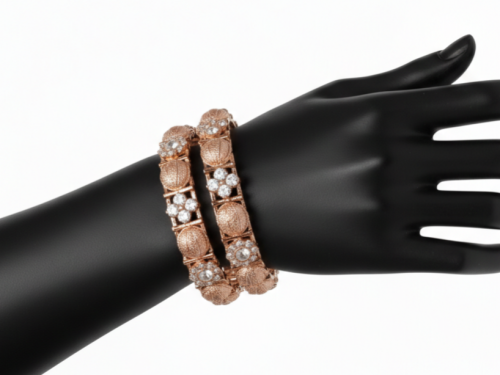 Two rose gold bangles displayed on a black mannequin hand. The design features alternating circular textured rose gold medallions and square settings containing four-petal floral clusters of white stones.