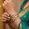 A pair of thick, two-tone bangles featuring a braided or wheat-link design in gold and frosted silver, accented with small embedded crystals. The bangles are worn on a wrist against a green and gold saree.