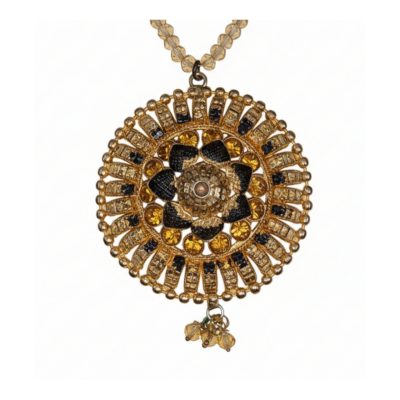 Detailed close-up of a circular gold sunburst pendant featuring an intricate flower center with black and amber gemstones on a beaded chain.