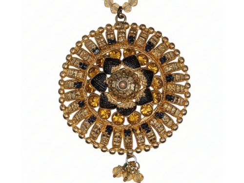 Detailed close-up of a circular gold sunburst pendant featuring an intricate flower center with black and amber gemstones on a beaded chain.