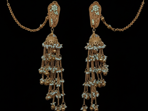 A pair of gold-toned Jhumka earrings displayed against a solid black background. The earrings feature sea-green beaded studs, a bell-shaped centerpiece, and multiple cascading chains adorned with tiny white beads and gold droplets. Long "Sahara" ear chains extend from the studs.